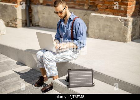 L'uomo lavora e carica il laptop da un pannello solare portatile Foto Stock