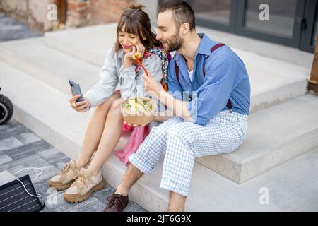 I colleghi mangiano cibo sano take away e parlano al telefono all'aperto Foto Stock