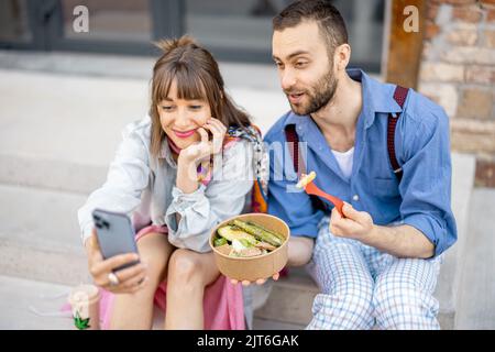 I colleghi mangiano cibo sano take away e parlano al telefono all'aperto Foto Stock