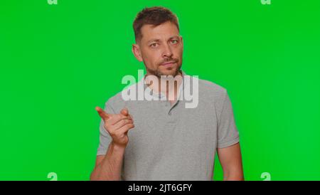 Il giovane dispiaciuto sconvolto scuote il dito e dice di no, stai attento, cogliendo e dando consigli per evitare errori di pericolo, segno di disapprovazione. Ragazzo di stile adulto isolato su sfondo chiave croma verde Foto Stock