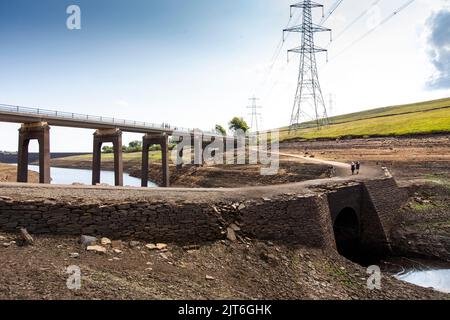 Ripponden, West Yorkshire, UK, 28th agosto 2022 UK Weather Baitings Dam è al suo livello più basso nella memoria recente. Il bacino idrico dello Yorkshire vicino a Ripponden è così asciutto che l'antico ponte a cavallo è stato esposto - sommerso da quando il bacino fu inondato negli anni '1950s - e il letto di quello che un tempo era un lago ora assomiglia ad un paesaggio desertico. Baitings è diventato un'attrazione turistica nelle ultime settimane, poiché i livelli nazionali delle acque nei serbatoi sono scesi al loro livello più basso dal 1995. Credit: Windmill Images/Alamy Live News Foto Stock