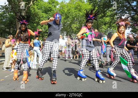 Londra, Regno Unito. 28th ago, 2022. Un gruppo incluso sui pattini a rotelle e in carrozzina davanti alla parata esegue acrobazie e intrattiene la folla. I partecipanti posano e Buon divertimento. La giornata della famiglia si svolge al Carnevale di Notting Hill con carri, bande d'acciaio e gruppi di danza che celebrano il ritorno del carnevale. Ci si aspetta che oltre un milione di persone partecipino a quello che quest'anno è considerato il più grande evento di strada in Europa. Credit: Imageplotter/Alamy Live News Foto Stock
