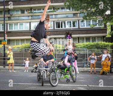 Londra, Regno Unito. 28th ago, 2022. Un gruppo incluso sui pattini a rotelle e in carrozzina davanti alla parata esegue acrobazie e intrattiene la folla. I partecipanti posano e Buon divertimento. La giornata della famiglia si svolge al Carnevale di Notting Hill con carri, bande d'acciaio e gruppi di danza che celebrano il ritorno del carnevale. Ci si aspetta che oltre un milione di persone partecipino a quello che quest'anno è considerato il più grande evento di strada in Europa. Credit: Imageplotter/Alamy Live News Foto Stock