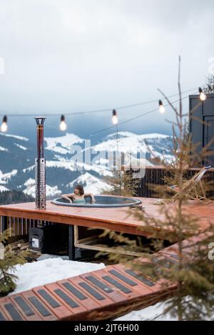 La donna nuota nel bagno caldo mentre riposa in una piccola casa moderna in montagna Foto Stock