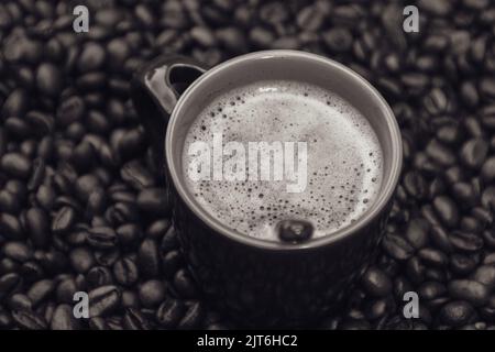 Una foto in scala di grigi di una tazza di caffè e chicchi di caffè Foto Stock