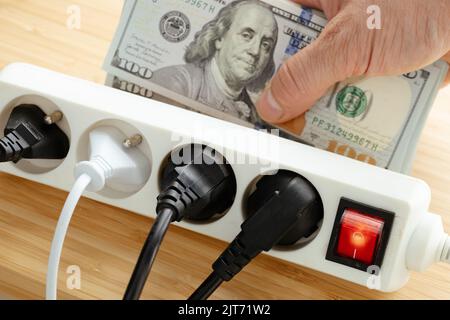 Aumenti dei prezzi dell'elettricità negli Stati Uniti, Energy Concept, Power Strip con spine collegate e un grande pacchetto di dollari in mano, increas Foto Stock
