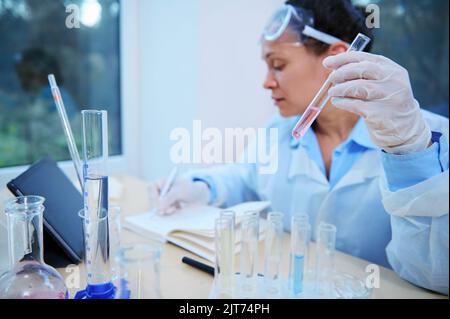 Provetta con soluzione, a mano dello scienziato, per annotare i risultati dello studio clinico, condotta in laboratorio scientifico Foto Stock