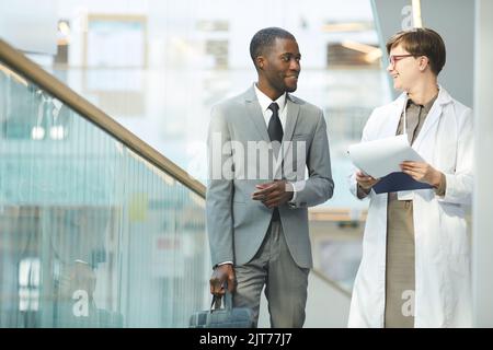 Ritratto di uomo d'affari nero sorridente che parla con una collega, mentre si cammina verso la macchina fotografica nella sala dell'edificio di uffici, spazio copia Foto Stock