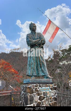 nagasaki, kyushu - 14 2021 dicembre: Statua del samurai Sakamoto Ryōma con kimono e spade katana a parte la sua bandiera della compagnia di navigazione Kaientai Foto Stock