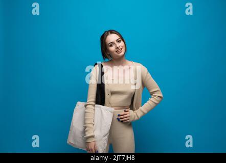 Bella donna brunetta in costume beige con sacco di cotone a spalla su sfondo blu. Concetto di mockup e zero sprechi. Foto Stock