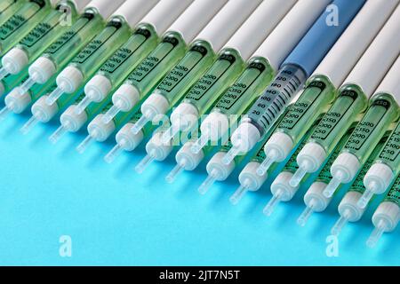 Penne per insulina diabetica allineate su uno sfondo blu. Una siringa blu in una serie di siringhe grigie Foto Stock