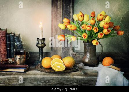 Classica vita morta con bouquet di tulipani fiori con arance fresche, sciarpa, libri d'epoca e candela illuminata su rustico tavolo in legno. Foto Stock