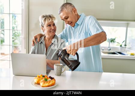 Coppia caucasica senior che ha fatto colazione utilizzando un computer portatile in cucina. Foto Stock