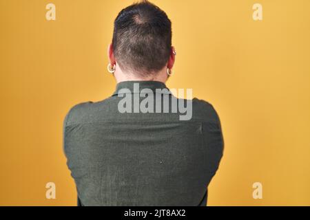 Uomo ispanico di taglia Plus con barba in piedi su sfondo giallo in piedi indietro guardando lontano con braccia incrociate Foto Stock