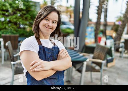 Giovane giù sindrome donna sorridente sicuro indossare grembiule al bar terrazza Foto Stock