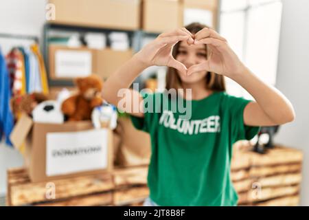 Adorabile ragazza che indossa uniforme volontaria facendo il simbolo del cuore con le mani al centro di carità Foto Stock