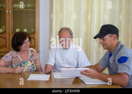 Immagine di una coppia anziana che controlla i documenti e le fatture di un lavoratore di costruzione per il lavoro domestico di rinnovamento. Foto Stock