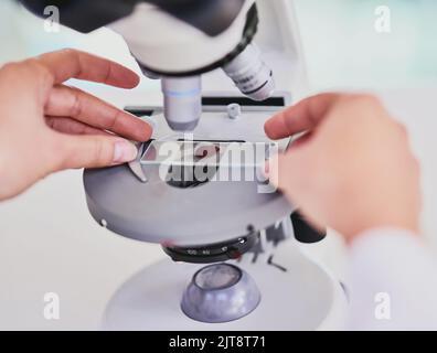 Tempo necessario per esaminare un nuovo campione. Primo piano di uno scienziato utilizzando un microscopio mentre si è seduti in un laboratorio. Foto Stock