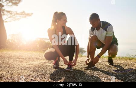 Si motivano a vicenda per muoversi. Una giovane coppia in forma che lega i loro lacci prima di una corsa all'aperto. Foto Stock