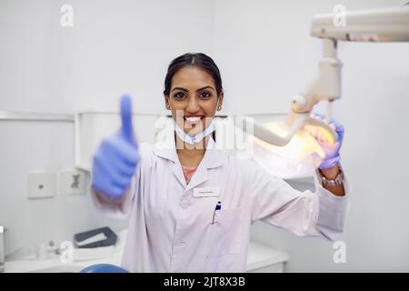 Qui per aiutarvi a mantenere una buona salute orale. Ritratto di una giovane dentista che mostra i pollici nel suo ufficio. Foto Stock