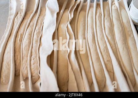 Il processo di fabbricazione di baguette francesi tradizionali in un panificio artigianale. Pane di prova su tessuto. Vista frontale. Foto Stock