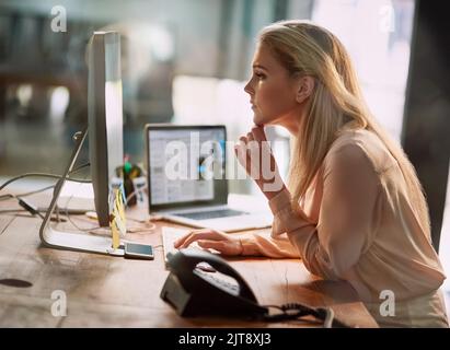 Shes il primo in ufficio e ultimo fuori. Una giovane donna d'affari concentrata che lavora su un computer in un ufficio. Foto Stock