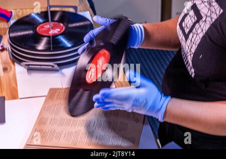 22 agosto 2022, Meclemburgo-Pomerania occidentale, Güstrow: I dipendenti della società discografica 'questione di fatto' controllano e imballano i record appena pressati nelle loro copertine. (L'azienda, che attualmente impiega cinque persone, produce record per diverse settimane in un ex locale per la patata, che ha dovuto essere ampiamente convertito per la produzione da record. Con una forza di 150 tonnellate, le lunghe registrazioni sono prodotte da cloruro di polivinile (PVC) sulle presse a 200 gradi Celsius. Ogni anno devono essere premuti tra 250.000 e 300.000 record. Secondo l'Associazione tedesca dell'industria musicale, Foto Stock