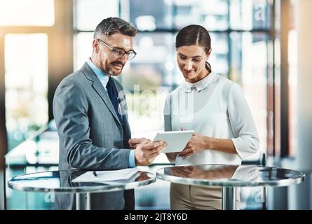 La tecnologia moderna è al passo con le esigenze delle aziende moderne. Due colleghi utilizzano un tablet digitale insieme in un ufficio moderno. Foto Stock