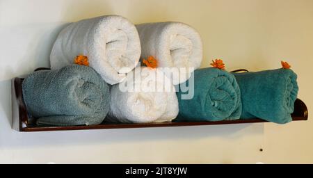 Sei asciugamani arrotolati in una mensola da bagno con pochi fiori arancioni Foto Stock