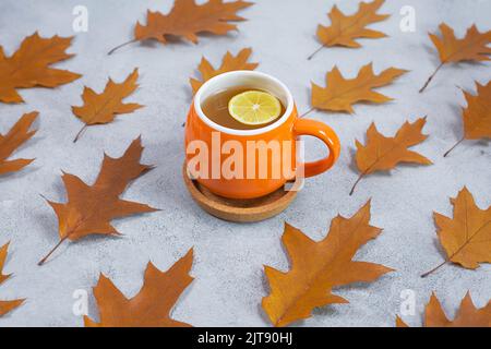 Foglie di quercia secca e una tazza di tè al limone su fondo grigio in cemento. Composizione autunnale. Autunno, Pattrern Autunno. Piano di giacitura, vista dall'alto. Foto Stock