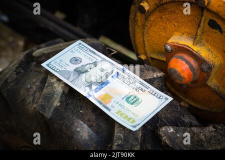 Un centinaio di dollari per primo piano si trovano sulla ruota di un trattore a piedi. Il denaro si trova su uno pneumatico con un grande battistrada nel fango. Finanziamento dell'agricoltura Foto Stock