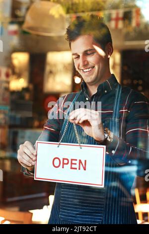 Im aperto al lavoro. Primo piano di un giovane uomo che appende un cartello aperto in una vetrina. Foto Stock