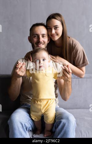 I genitori e il loro figlio sedersi rannicchiato nella stanza vivente e sorridente Foto Stock