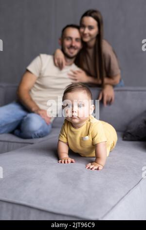 I genitori e il loro figlio sedersi rannicchiato nella stanza vivente e sorridente Foto Stock