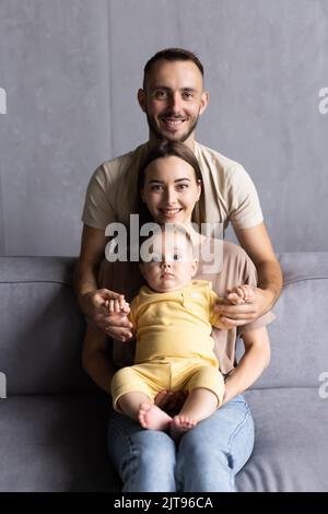 I genitori e il loro figlio sedersi rannicchiato nella stanza vivente e sorridente Foto Stock