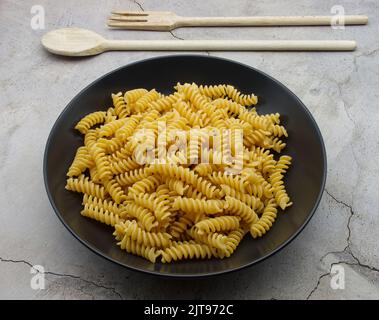 Fusilli Pasta italiana cruda in un piatto nero. Cucina tradizionale italiana. Foto Stock