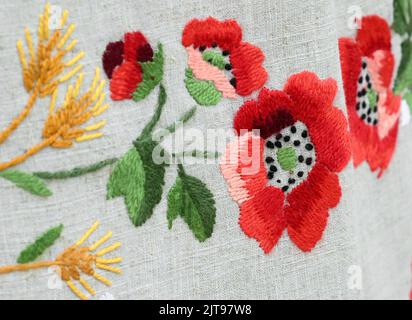 Primo piano ricamo tradizionale di fiori di papavero e spikelets di grano su tela di lino grigia Foto Stock