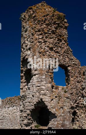 I buchi nelle pareti di una torre in rovina creano la somiglianza di un volto simile a un cranio con una bocca aperta sopra il fossato che difende il bailey interno del castello medievale di Pevensey nel Sussex orientale, Inghilterra, Regno Unito. Il castello fu costruito dai Normanni all'interno delle mura della fortezza costiera tardo romana di Anderitum. Foto Stock