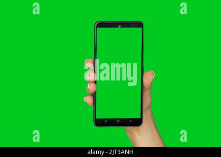 La mano di una donna su uno sfondo verde tiene un telefono cellulare con uno schermo verde, un modello con un telefono, uno schermo verde su un cellulare Foto Stock