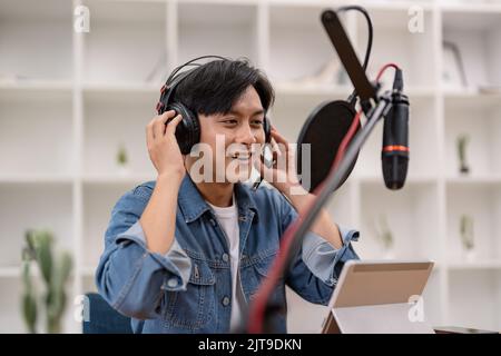 Podcaster maschile asiatico che produce podcast audio dal suo studio di casa Foto Stock