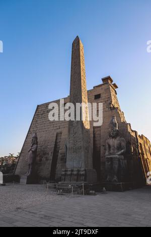 Vista al tramonto sulle statue di pietra illuminate del grande antico tempio egiziano a Luxor, Egitto Foto Stock