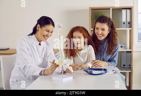 Felice medico, genitore e bambino che guarda il modello anatomico della colonna vertebrale e ridere Foto Stock