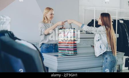 Il cliente allegro ha acquistato vestiti mentre si è in piedi alla scrivania del cassiere. L'assistente del negozio accetta di dare il suo sacchetto di carta. Foto Stock