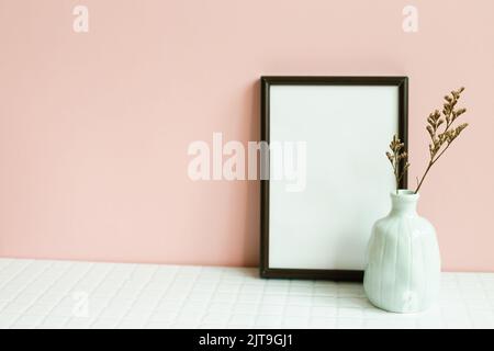 Decorazioni per interni in casa, cornice e vaso di pianta secca su tavolo bianco. Sfondo parete rosa Foto Stock