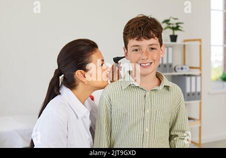 Otolaryngologist esamina un ragazzino felice e usa un otoscopio per controllare le orecchie Foto Stock