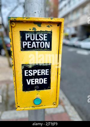 Un pulsante giallo di attraversamento pedonale a Madrid traduzione-premere per attraversare, attendere fino a quando la spia rossa si accende Foto Stock