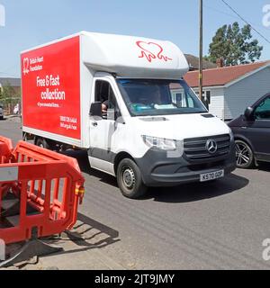 Logo di fronte alla British Heart Foundation rosso & bianco collezione caritatevole furgone fisso in strada residenziale breve ritardo lavori stradali Essex Inghilterra UK Foto Stock