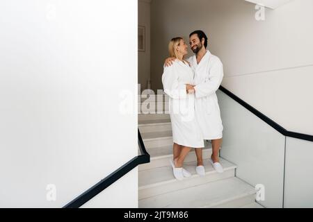 Bella coppia indossando accappatoi bianchi godendo il fine settimana spa mentre la luna di miele cammina al centro benessere Foto Stock