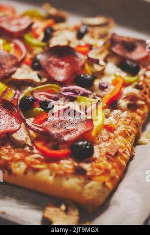 Un pezzo di pizza quadrata con pomodori peperoni al basilico e funghi su un vassoio di ferro servito con ingredienti freschi. Vista con disposizione piatta. Foto Stock