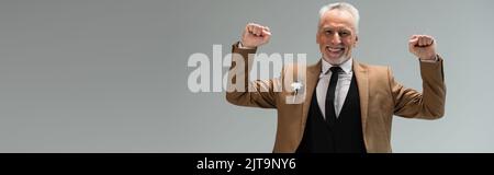 allegro sposo di mezza età in tuta con fiore boutonniere gesturing isolato su grigio, banner, immagine stock Foto Stock